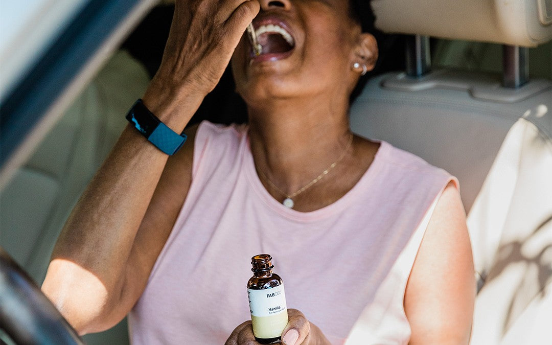A woman drops CBD oil under her tongue while sitting in the car