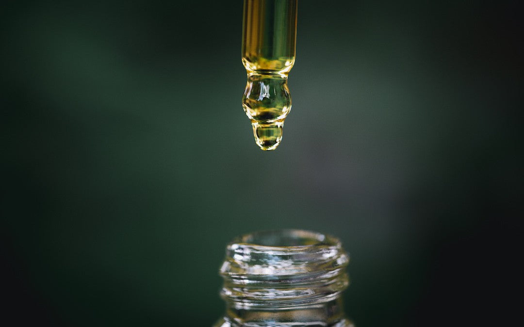 A close-up of CBD oil dripping from the dropper into the bottle