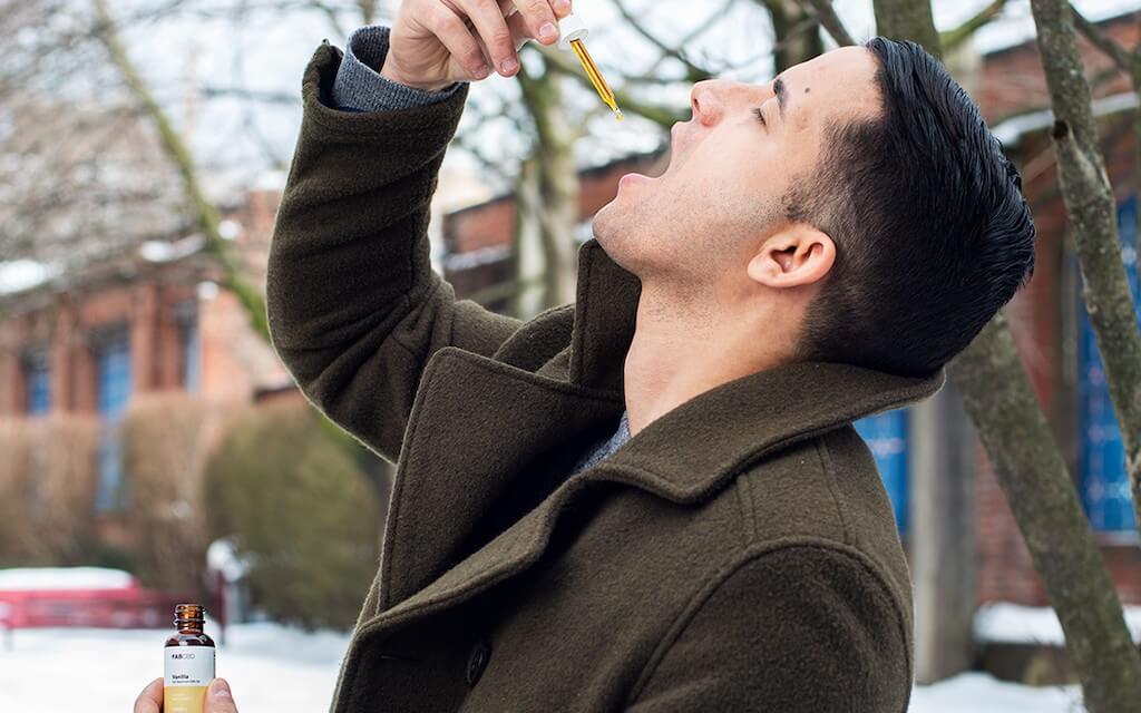 A young man drops CBD oil under his tongue while sitting outside