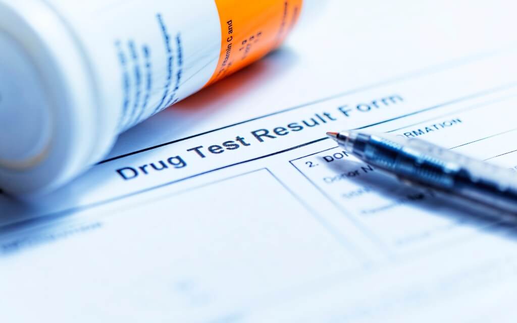 A prescription bottle lays over the corner of a blank drug test form and a pen rests atop the page.