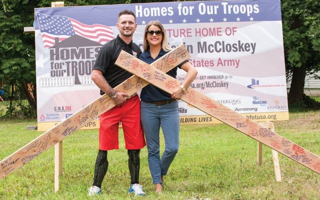 A Veteran and his partner hold building timber in front of a sign for Homes For Our Troops