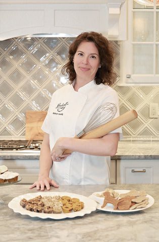 Woman standing with whiskand rolling pin in a white kitchen