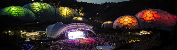 A music stage with the eden project in the background glowing green and orange