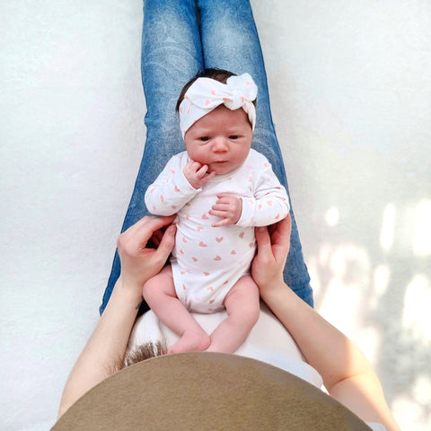 Újszülött kisbaba fehér bodyban fekszik az anyukája lábán