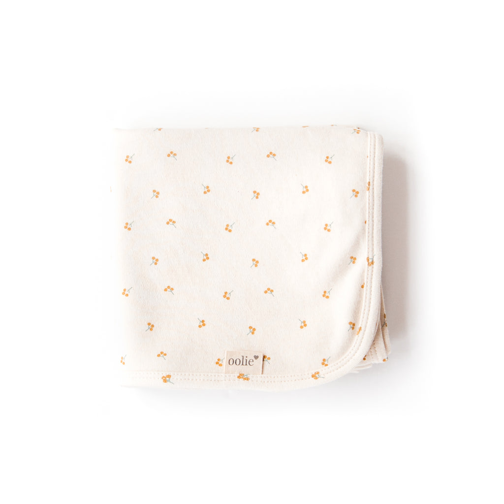 An Oolie organic cotton baby blanket with the gold sprig print, a natural color with small sprigs of golden berries.