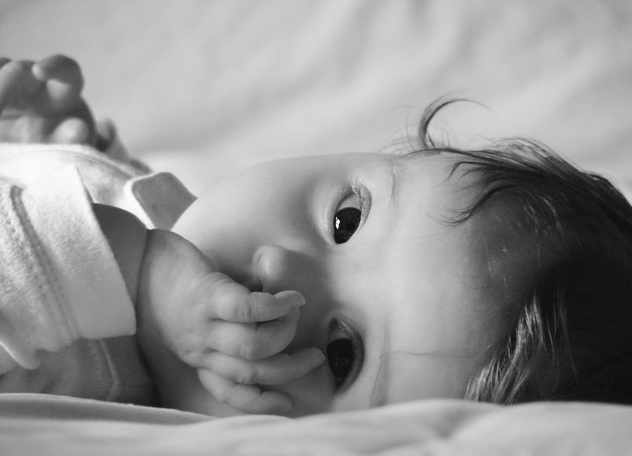 A baby resting in bed, awake but relaxed, looking at the camera.