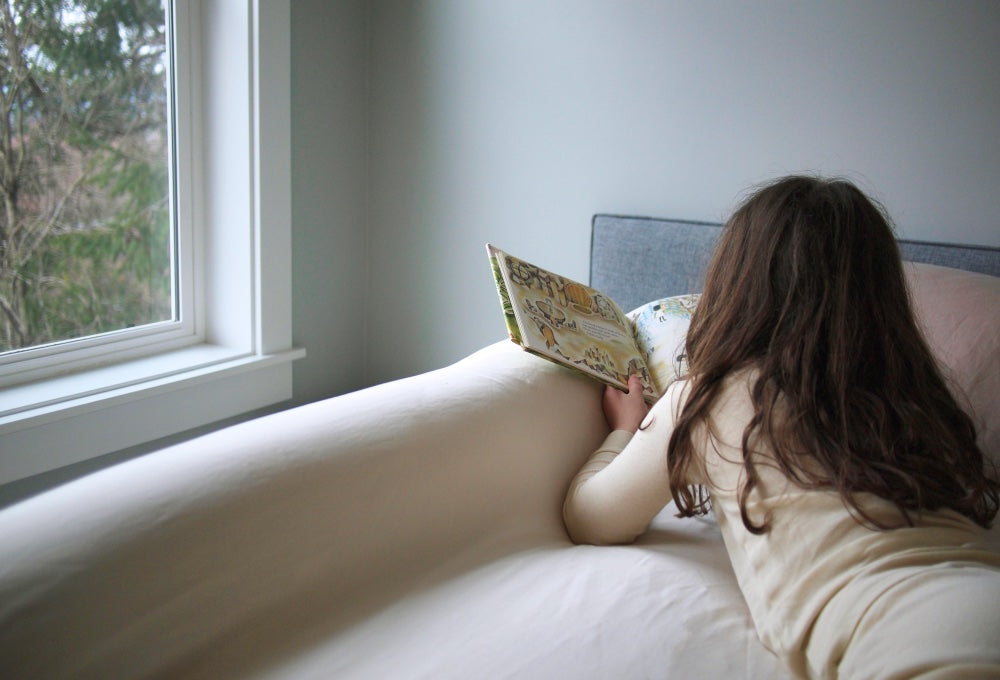 Girl reading in bed, snuggled against an Oolie Base