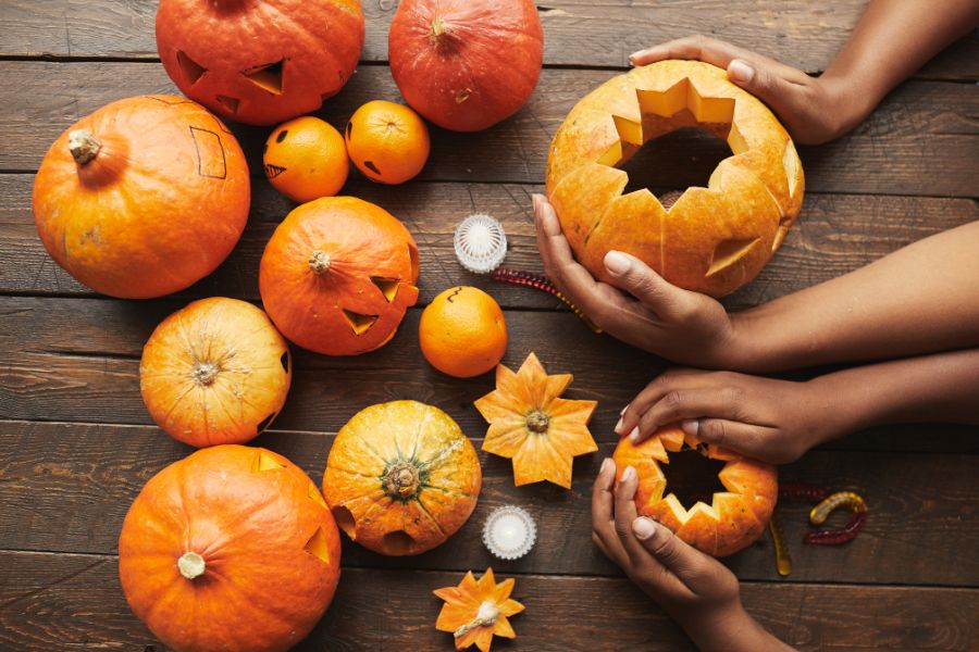 Hands holding carved pumpkins on a natural wooden table surface