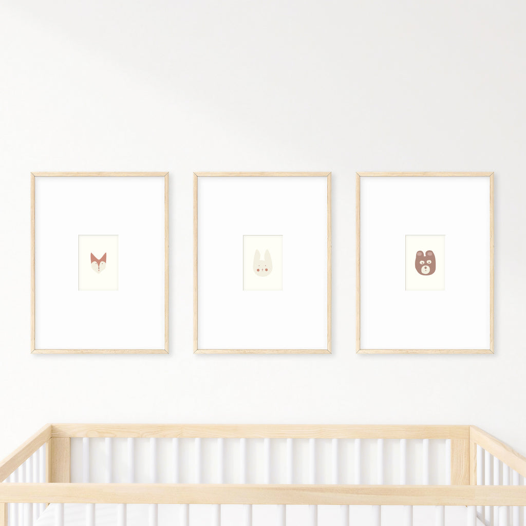 Three cute nursery prints framed and hanging on a wall over a baby's crib. The prints show: a fox, a bunny, and a bear, each in natural, soft colors.