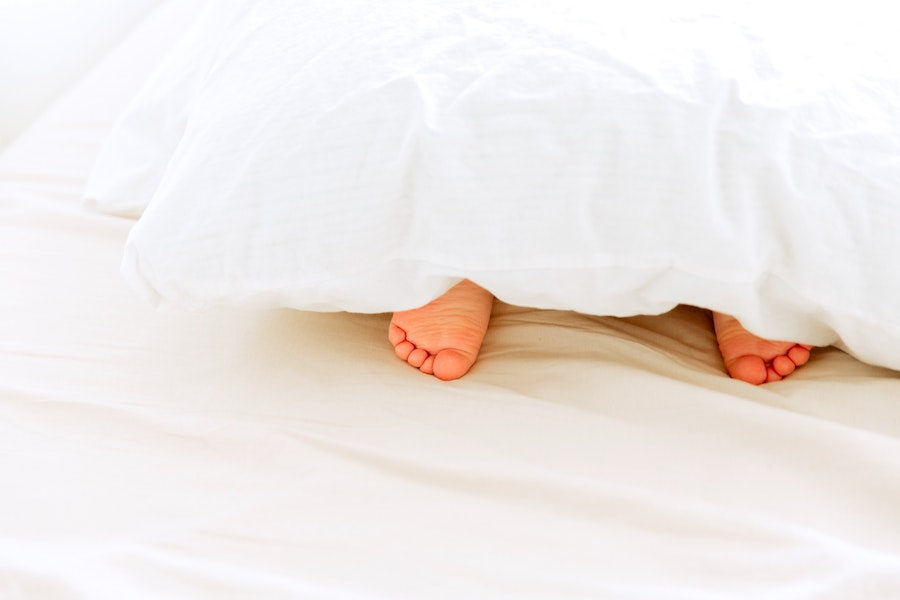 Two tiny feet of a young child peeking out from beneath white cotton covers on a bed.