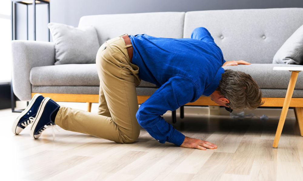 Man searching for something under his grey couch