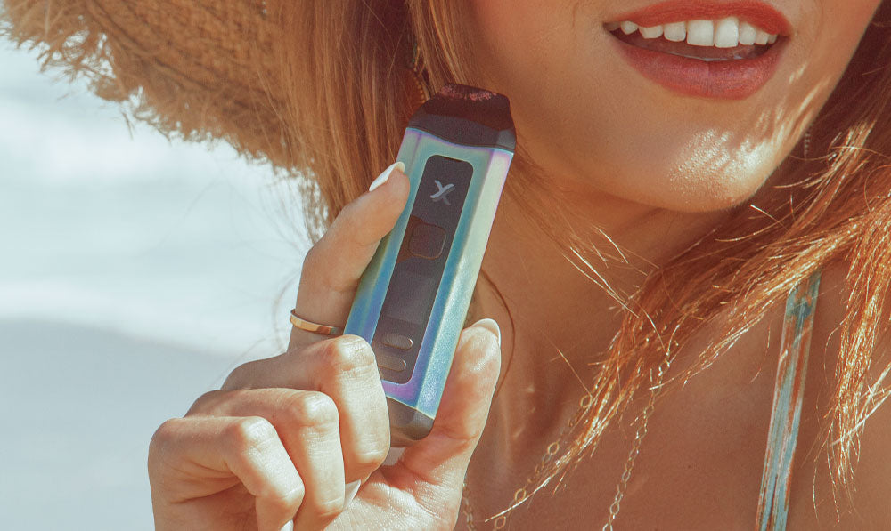 Woman in hat holding Exxus Mini Plus by the beach