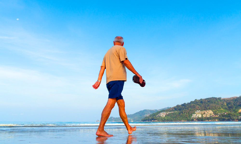 Senior man walking along a beach with clear blue skies