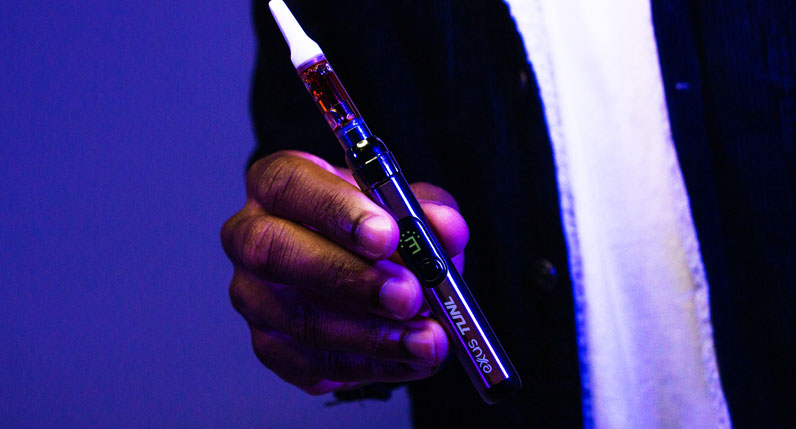 man with black jacket holding Exxus TUNL inside studio with blue background