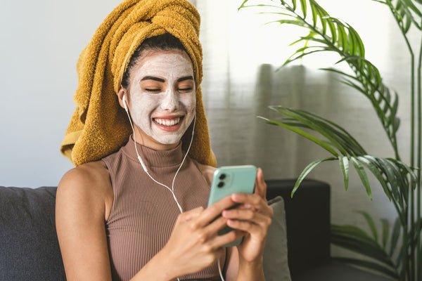 Foto de mujer usando su celular con mascarilla skincare día internacional de la relajación