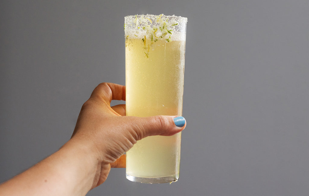 El Chonie cocktail being held, it is light in colour with a rim of salt and lime lemon