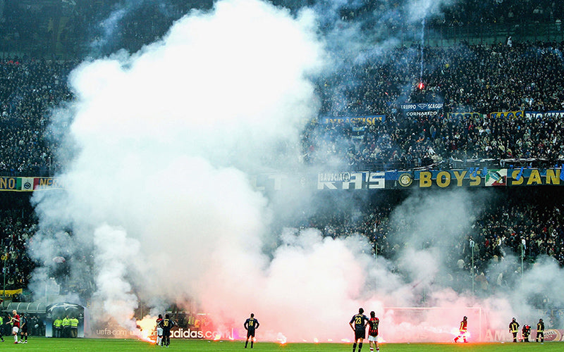 AC Milan and Inter Milan players watching their supporters lighting flares