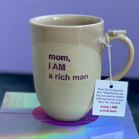 mug with purple text and pink tag from front. hang tag explains the story of cher telling her mom she doesn't need to marry a rich man because she is one.