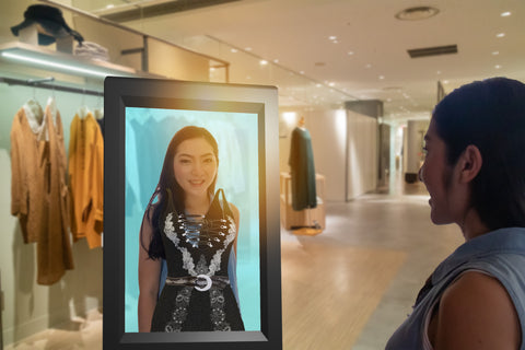 Woman in a retail clothing store looking at an image herself in an LED Display, where the image of a dress has been layered on top as if she were wearing it.