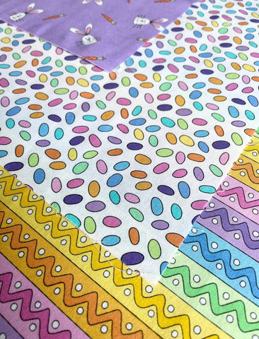 Hoppy Easter fabric by Kin Shaefer for Andover Fabrics. Purple with easter bunny heads, colorful little eggs on white, zigzag rainbow stripes.