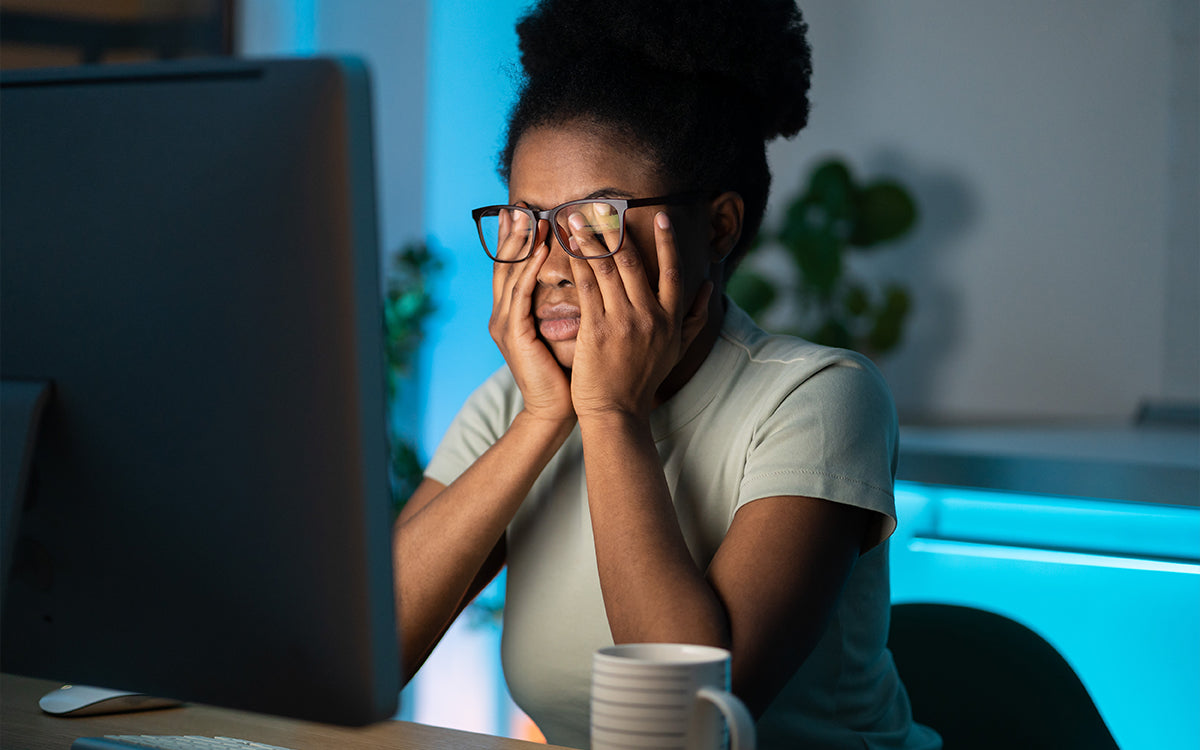 a woman rubbing her eyes in front of a computer