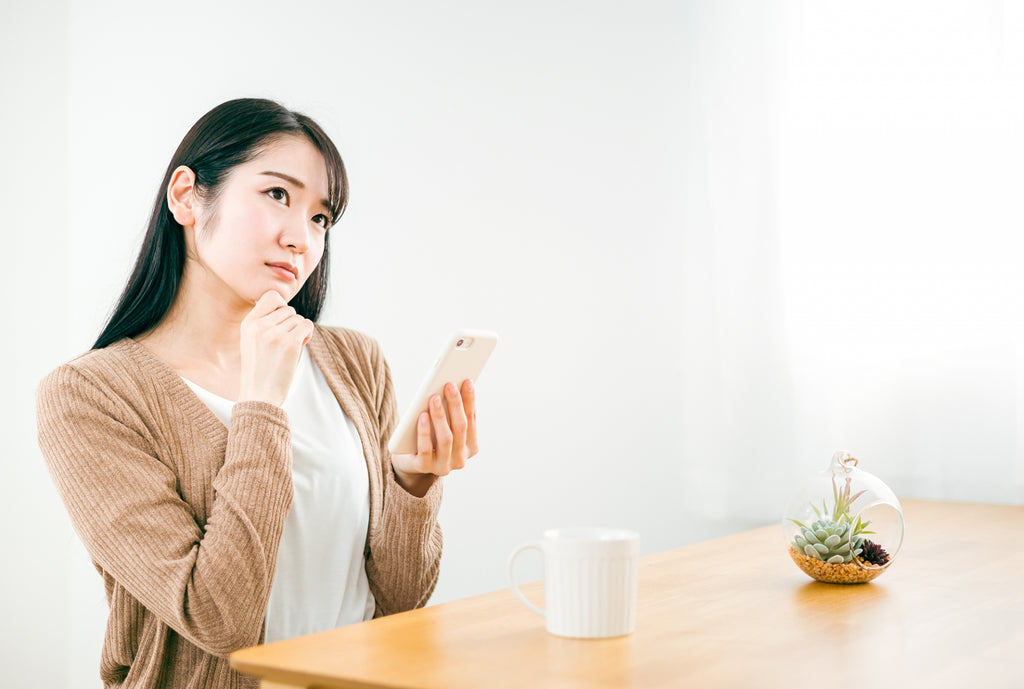 スマホを手に考える女性