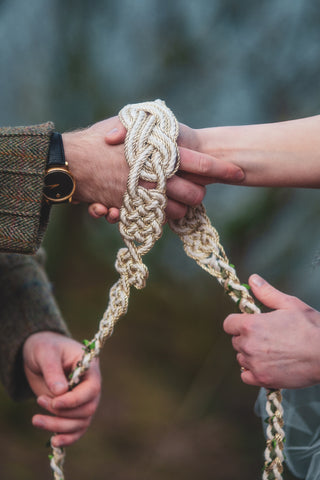 A couple tying a handfasting cord with the decorative centre knot shown at the top.
