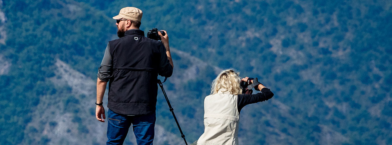 A woman wearing SCOTTeVEST Q.U.E.S.T photographer vest in black and holding a camera.