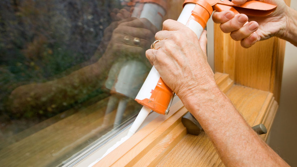man applying caulk on a window