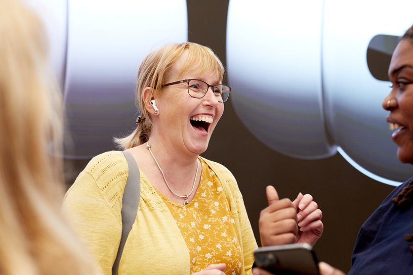 Mujer rubia sonriente con auriculares. Conoce las diferencias entre AirPods Pro 1 y 2.