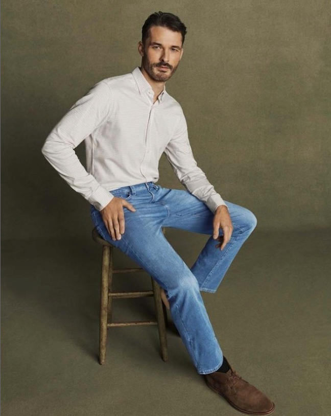 Alt text: Man sitting on a stool in coordinated outfit of a white button-down shirt and  medium-wash jeans