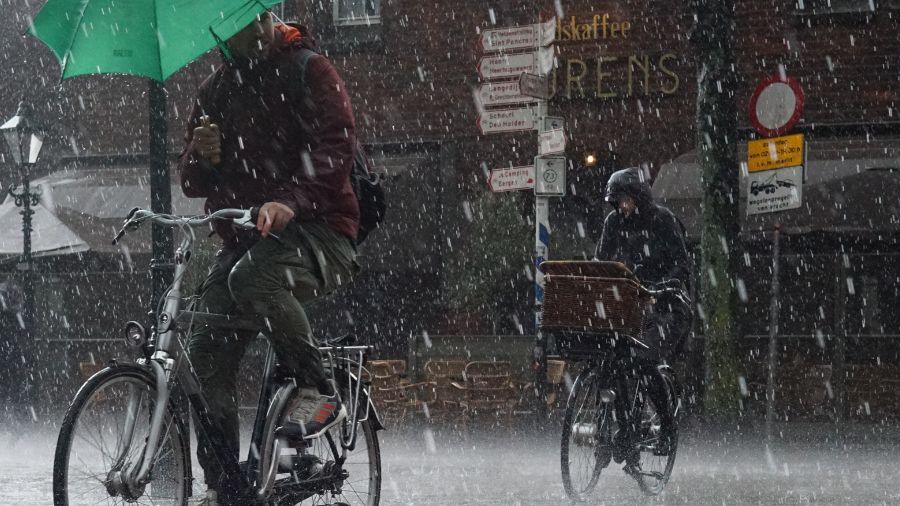 Deux cyclistes sous la pluie dans une rue, un des cyclistes tient un parapluie vert