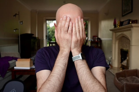 A bald man sitting at a desk buries his head in his hands in regret | how to start a journal