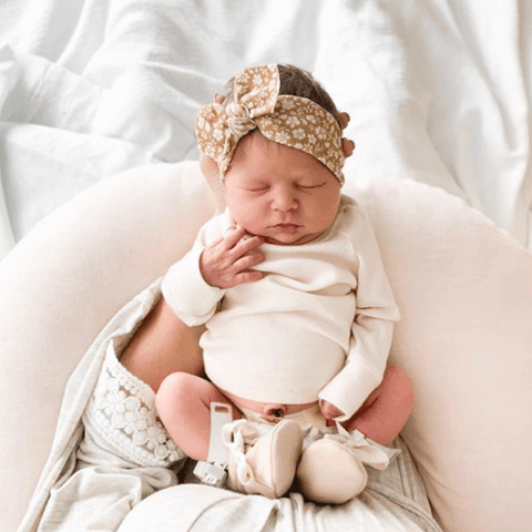 newborn baby in hospital laying on pink nursing pillow for girls