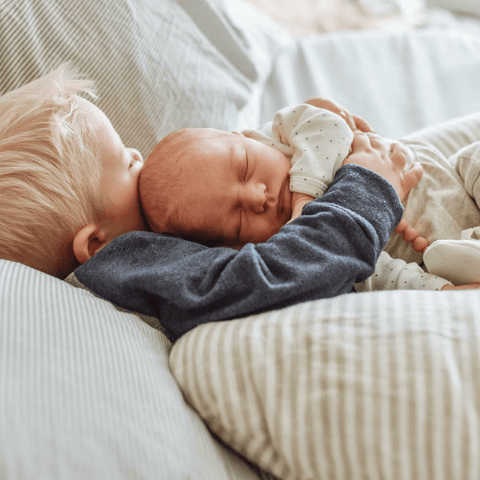 brother holding new baby with nursing pillow for support