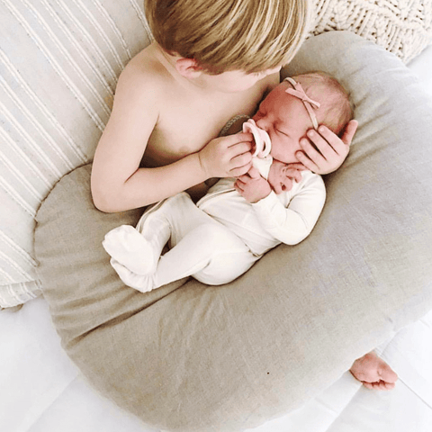 big brother holding new sister with a nursing pillow