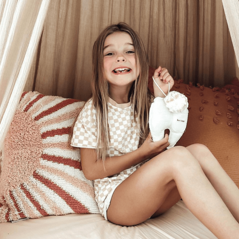 little girl sitting on her bed holding her personalized tooth pillow from madly wish