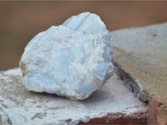 a raw blue calcite stone sitting on a brick ledge outdoors