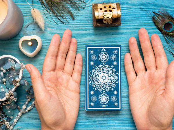 A person meditating with tarot cards on the table. There is blue calcite in a dish as well as a peacock feather.