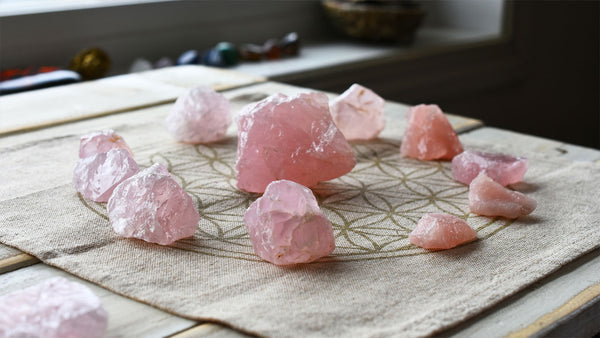 A variety of raw rose quartz crystal specimens, a healing stone, in a healing crystal grid are pictured.