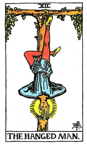 The Major Arcana card - the Hanged Man tarot card. A man is viewing the world from a different perspective by hanging upside down from one foot from a tree. His right foot is secured to the tree, while his left foot is left unbound, bent at the knee, and tucked behind his right leg. His arms are bent, with hands positioned behind his back, creating an inverted triangle.
