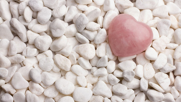 A tumbled rose quartz heart on top of white quartz stone chips.