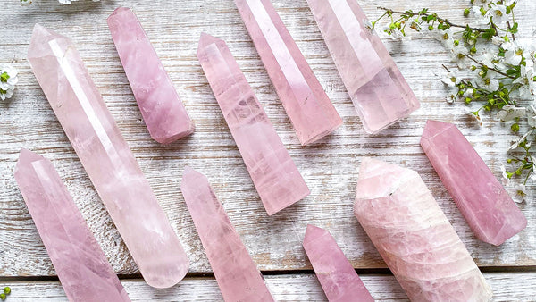 A pale pink stone vaeof Rose Quartz is displayed. There are several rose quartz towers on a table.