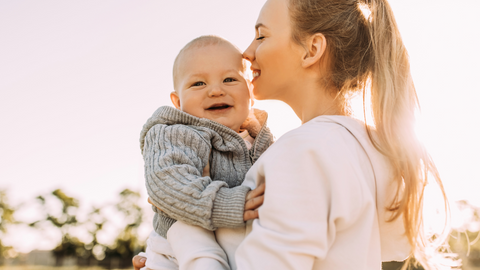 mom holding and kissing baby outside