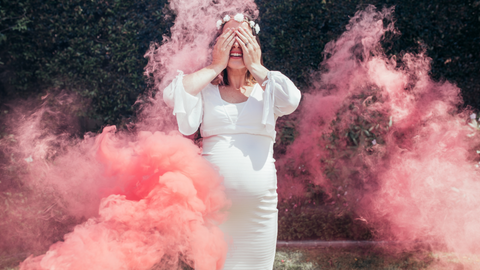 gender reveal powder in the air with pregnant woman closing her eyes