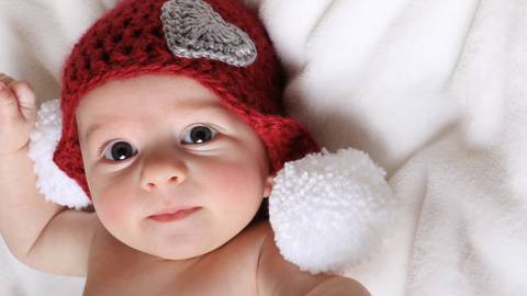 baby with valentines day beanie laying on bed