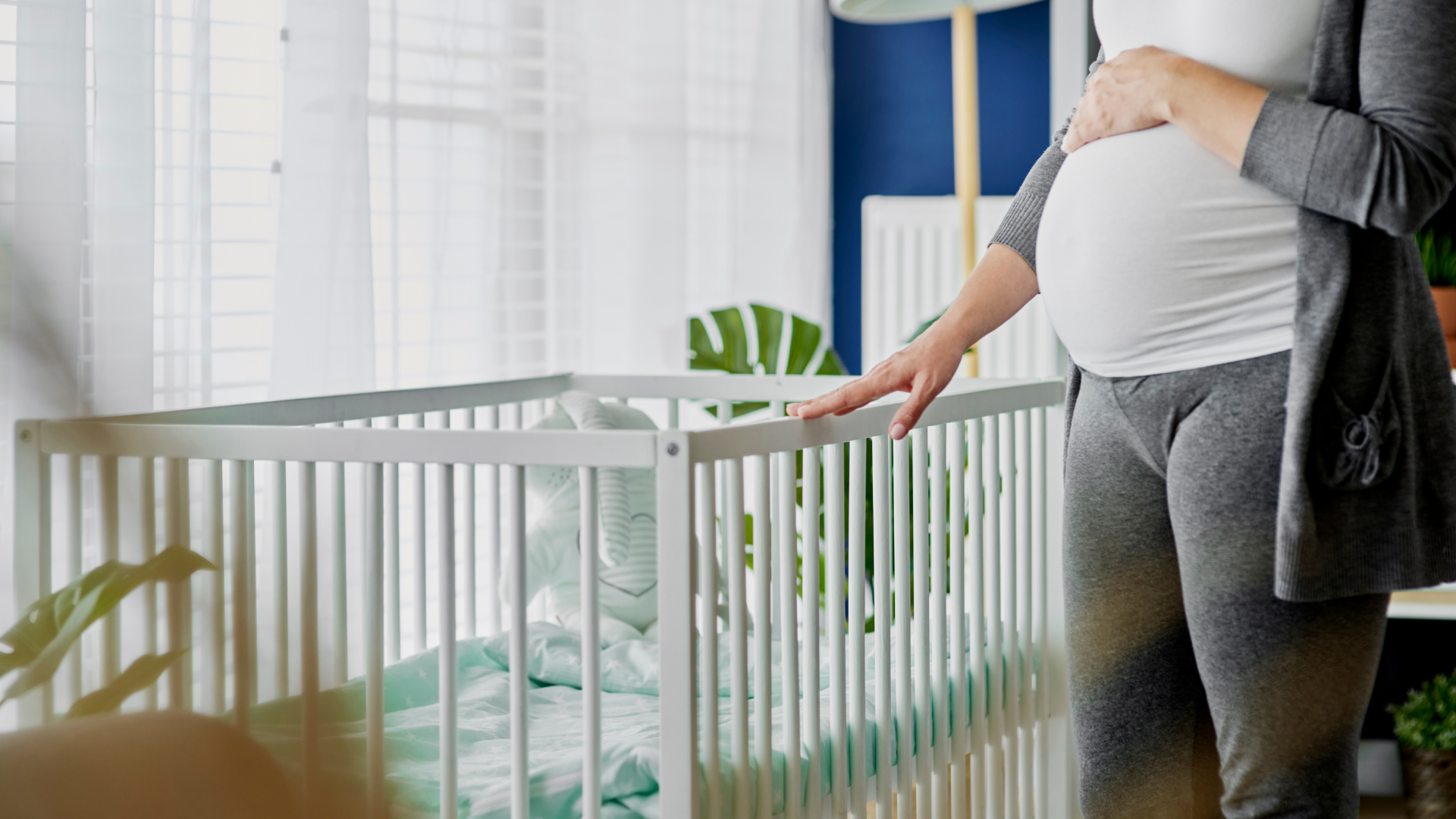 pregnant lady with hand on cot in nursery