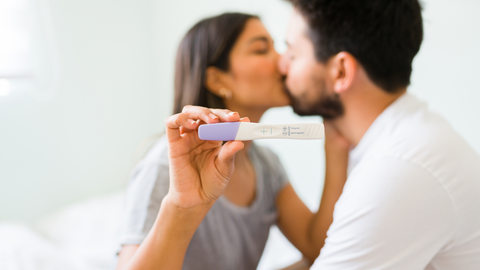 couple kissing and holding pregnancy test