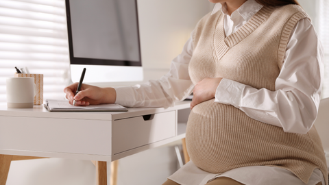 pregnant woman writing memories in paper baby book