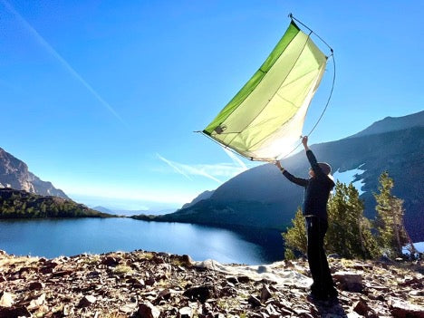 person setting up a tent on the shore of a lake